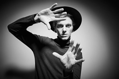 Stüdyoda şık kıyafetler ve şapkayla poz veren zarif bir gencin siyah beyaz portresi. Moda fotoğrafı..