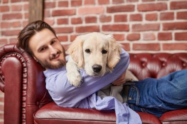 Evcil köpeği Golden Retriever ile evdeki kanepede yatan mutlu genç adam. Bir adam ve bir evcil hayvan.