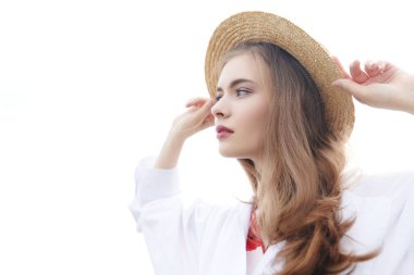 Açık beyaz gömlekli ve şapkalı güzel romantik kız parlak gökyüzüne karşı duruyor. Yaz tatili.