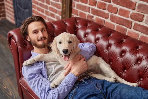 Bir adam ve bir evcil hayvan. Mutlu genç adam evcil köpeği Golden Retriever ile kanepede yatıyor..
