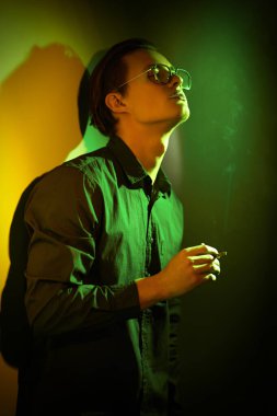 Genç adam koyu yeşil ve sarı ışıkta sigara içiyor. Kötü alışkanlıklar. Sigara molası..