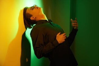 Duygular ve duygular. Duygusal genç adam duruyor, üzgün ve yalnız, duvara yaslanmış koyu yeşil ve sarı ışıkta.