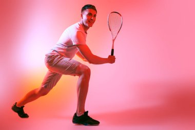 Aktif bir sporcunun tam boy portresi. Karmaşık renkli ışıkla squash oynayan. Etkin yaşam tarzı, spor ve sağlık hizmetleri. 