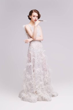 Ağızlıkta sigara içen lüks beyaz elbiseli güzel ve şık bir genç kadının tam boy portresi. Moda fotoğrafı. Gelinlik. Hollywood tarzı.