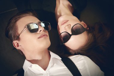 Modern güneş gözlüklü kadın ve erkeğin portresi lüks bir dairede kanepede yatıyor. Moda fotoğrafı. Göz kamaştırıcı yaşam tarzı. 