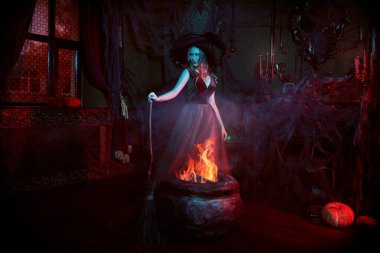 Cadılar Bayramı 'nda peri masalları. Büyüleyici genç cadı, süpürgeyle eski bir şatoda kazanın yanında poz veriyor.. 