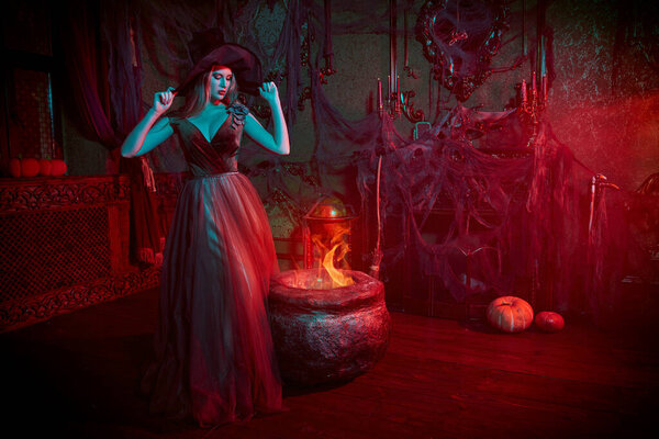 Enchanting young witch conjures over the cauldron in an old castle. Fairy tales on Halloween.