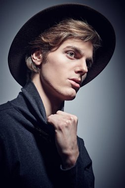 Geniş kenarlı şapkalı ve balıkçı yaka kazaklı yakışıklı bir genç. Gri arkaplanda stüdyo portresi. 