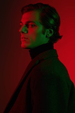 Stüdyoda kırmızı ve yeşil ışıkta poz veren zarif elbiseli yakışıklı bir adamın portresi. Erkek güzelliği. Moda..