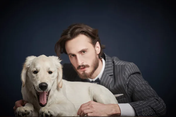 Fashion, man and dog. Portrait of a handsome man in elegant suit posing with a Golden Retriever puppy on a black background.