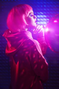 Parlak makyajlı ve gece kulübünün neon ışıklarında poz veren pembe saçlı modern bir kız portresi. Disko biçimi. 