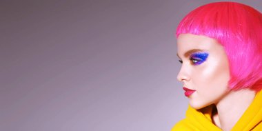 Parlak makyajlı, pembe saçlı, şık sarı elbiseli bir model stüdyoda poz veriyor. Makyaj ve saç stili. Spor şık kıyafetler. Parti biçimi.