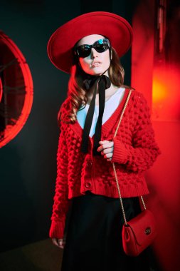 Zarif kırmızı şapka, hırka ve moda güneş gözlükleriyle poz veren güzel bir manken kızı portresi. Yeni kıyafet koleksiyonu. Optik biçimi.