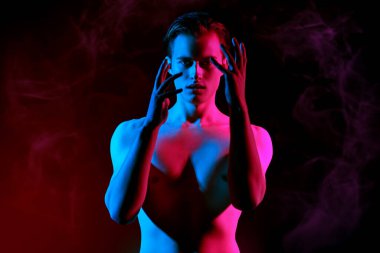 Sanat portresi. Mavi ve kırmızı ışıkta poz veren kaslı çıplak gövdeli yakışıklı genç adam. İnsanın güzelliği ve sağlığı. 