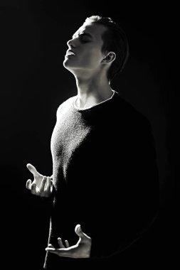 Siyah-beyaz bir portre. Acı çeken genç bir adam. Karanlık ışıkta duruyor. Erkek güzelliği. Siyah arkaplan. 