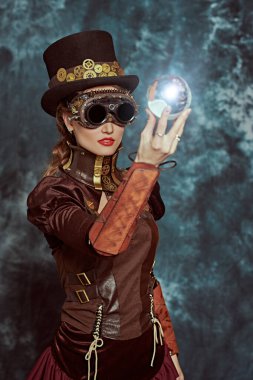 Victoria döneminden kalma güzel bir steampunk bayan, arka planda enerji kristali topunu tutuyor. Fantezi dünyası, bilimsel icatlar.