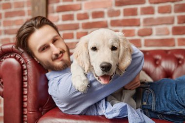 Bir adam ve bir evcil hayvan. Mutlu genç adam evcil köpeği Golden Retriever ile kanepede yatıyor..