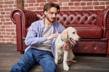 Mutlu sakin genç adam yerde oturuyor ve köpeğine sarılıyor..