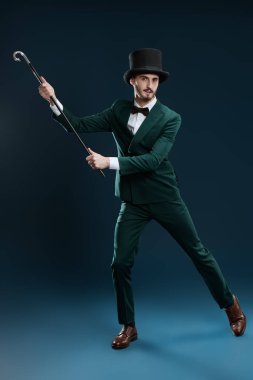 Elegant gentleman in suit and top hat dances with a cane. Studio portrait on a dark blue background. Men's fashion.  clipart