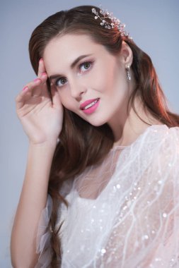 Düğün makyajı ve saç stili. Zarif beyaz gelinlik içinde güzel bir gelinin portresi. Gri arkaplanda stüdyo portresi.