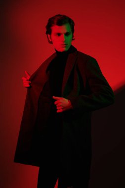 Erkek tarzı. Stüdyoda kırmızı ışıkta poz veren zarif elbiseli yakışıklı bir gencin portresi..