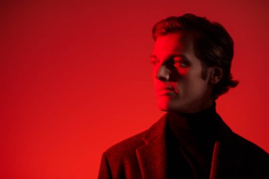 Stüdyoda kırmızı ışıkta poz veren şık giyinmiş yakışıklı bir adamın portresi. Erkek güzelliği. Moda. Boşluğu kopyala.