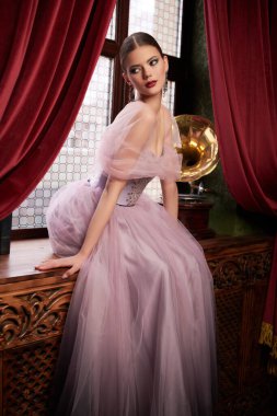 Pofuduk uzun elbiseli güzel romantik bayan lüks bir apartmanın pencere eşiğinde oturuyor. İç mekan, moda.