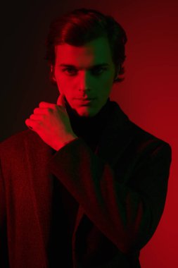 Stüdyoda kırmızı ve yeşil ışıkta poz veren zarif elbiseli yakışıklı bir adamın portresi. Erkek güzelliği. Moda..