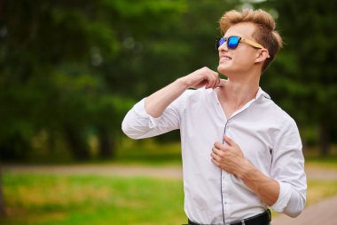 Yakışıklı genç adam parkta yürüyor ve gülümsüyor. Yaz modası. Yaz tatili ve tatil.