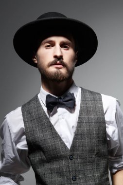 Zarif klasik takım elbiseli yakışıklı bir esmer adam portresi ve gri arka planda siyah bir şapka. Erkek güzelliği. Moda..