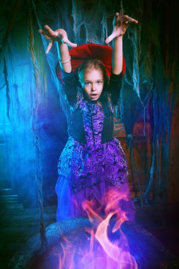 Eski evdeki yanan kazanda bir cadının kostümünü giyen sevimli küçük bir kız. Cadılar Bayramı.