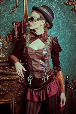 Steampunk dünyası. Victoria döneminden kalma iç mimarisi olan bir odada şöminenin yanında duran güzel bir steampunk bayanın portresi.. 