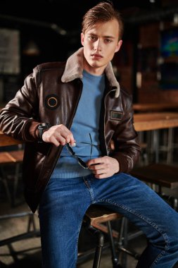 Deri ceketli ve kot pantolonlu şık bir genç adam bir barda vakit geçiriyor. Erkek modası. Yaşam biçimi. 