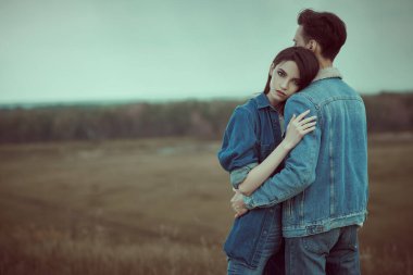 Denim tarzı. Kot elbiseli dramatik bir çift genç vadide durmuş fırtınalı bir gökyüzüne sarılıyorlar. Güzellik, moda. İlişkiler.