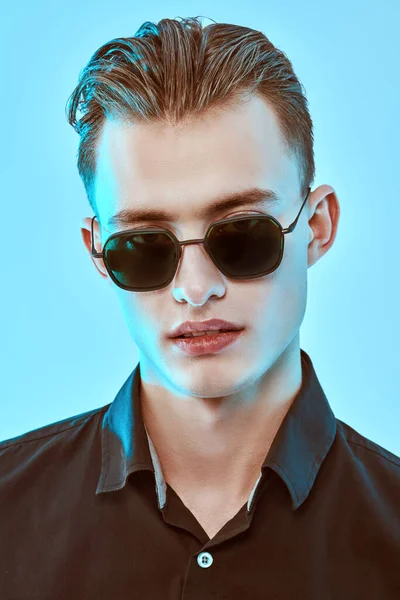 Portrait of a handsome young man in black shirt and stylish sunglasses on a blue background. Men\'s fashion. Accessories, optics.