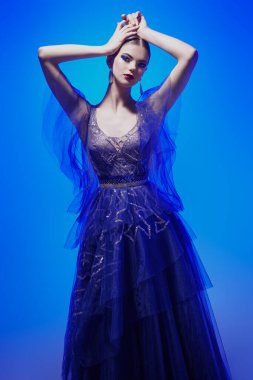 Akşam modası. Güzel, zarif bir manken, şık bir gece elbisesiyle karışık renkli bir ışıkla poz veriyor. Stüdyo resmi. 