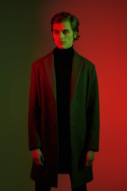 Stüdyoda kırmızı ve yeşil ışıkta poz veren zarif elbiseli yakışıklı bir adamın portresi. Erkek güzelliği. Moda..