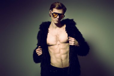 Şık bir genç adamın portresi. Şık bir güneş gözlüğü ve çıplak bir gövdeye giydirilmiş kürk manto. Moda yıldızı adam.. 