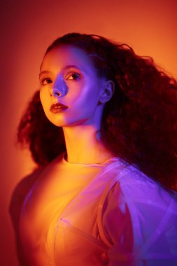 Moda sanatı. Beyaz bir sanat elbisesi içinde poz veren gür kırmızı kıvırcık saçlı güzel bir kadın model. Renkli bir stüdyo portresi..