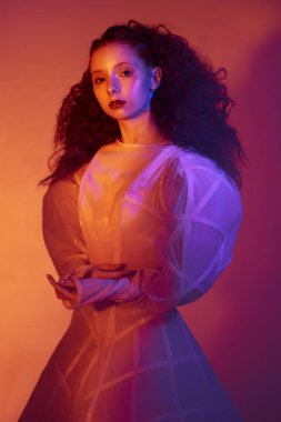 Moda sanatı. Beyaz bir sanat elbisesi içinde poz veren gür kırmızı kıvırcık saçlı sofistike bir kadın modelin portresi. Renkli bir stüdyo portresi..