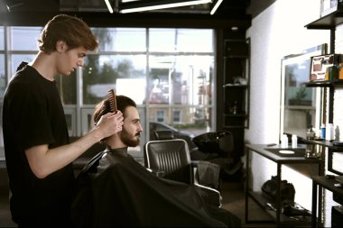 Yakışıklı esmer adam berber dükkanında bir sandalyede otururken kuaföre saç kestiriyor.. 