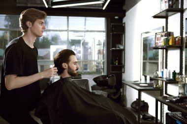 Berber berber dükkanında çalışıyor. Koyu saçlı, sakallı ve bıyıklı yakışıklı adamın kuaför salonunda saç kesimi var.. 