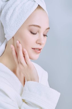 Güzellik, vücut bakımı, spa. Beyaz bornozlu güzel bir genç kadın portresi ve duş aldıktan sonra saçının etrafına bir havlu.. 