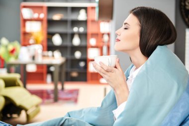 Güzel, mutlu kız, rahat, aydınlık salonunda dinleniyor. Oturur, battaniyeye sarılır ve sıcak çay içer. Mutlu insanlar ve yaşam tarzı konsepti.