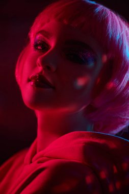 Makyaj ve saç stili. Parlak makyajlı, pembe saçlı, neon ışıkta poz veren modaya uygun bir manken kızı portresi. Güzellik eğilimleri. 