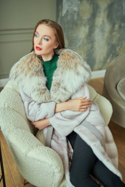Kürk manto modası. Pahalı vizon kürklü ve vaşak kürklü güzel sarışın kadın klasik lüks bir iç mekanı olan bir dairede poz veriyor.. 