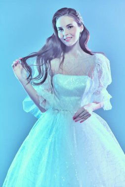 Düğün stili. Lüks beyaz elbiseli, yumuşak mavi ışıklı güzel bir gelinin portresi. Düğün makyajı ve saç stili.