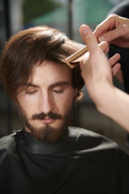 Bir berber dükkanında saçını kestiren yakışıklı bir esmerin yakın plan portresi. Erkek güzelliği ve tarzı. 