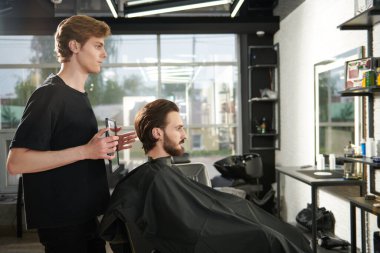 Yakışıklı esmer adam berber dükkanında bir sandalyede otururken kuaföre saç kestiriyor.. 