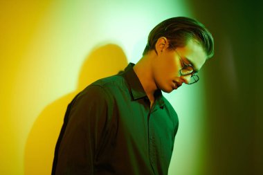 Duygular ve duygular. Yakışıklı genç adam duruyor, üzgün ve yalnız, duvara yaslanmış koyu yeşil ve sarı ışıklı. 